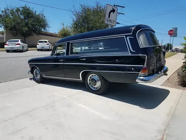 Black vintage hearse parked on a sunny street corner near a stop sign