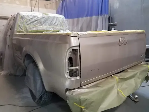 Silver pickup truck in a paint booth, masked with plastic and paper for bodywork repair