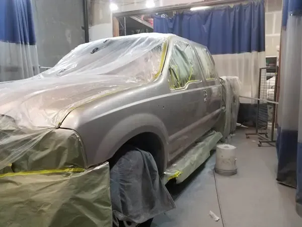 SUV covered in plastic in an auto body shop, surrounded by masking paper and paint equipment