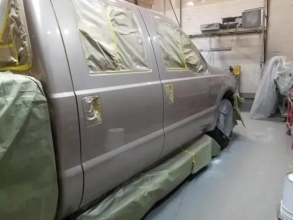 Gray SUV masked with plastic and tape in an auto body paint booth