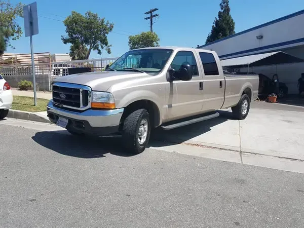 Beige pickup truck parked in a driveway beside a building on a sunny street.