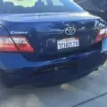 Rear view of a dark blue Toyota sedan with a visible license plate and snowy ground behind it