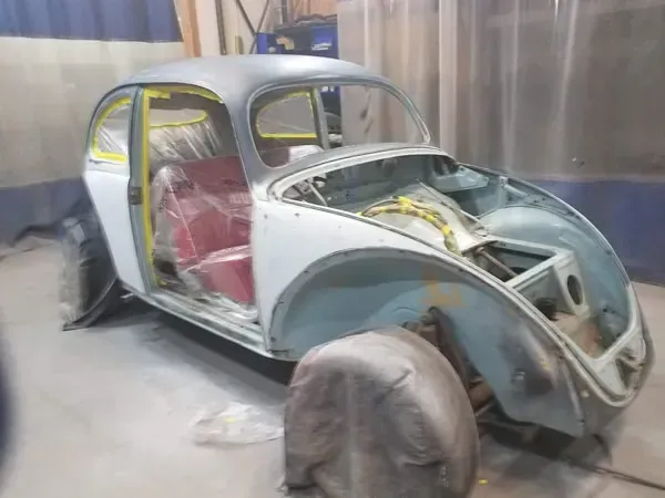 Old car body in a workshop, partially restored and masked for painting, with exposed frame and red seats