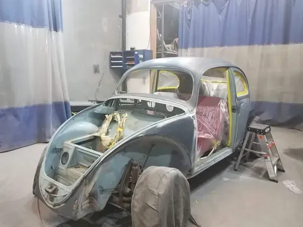 Partially restored vintage car body in a workshop, with blue and silver paint and exposed interior.