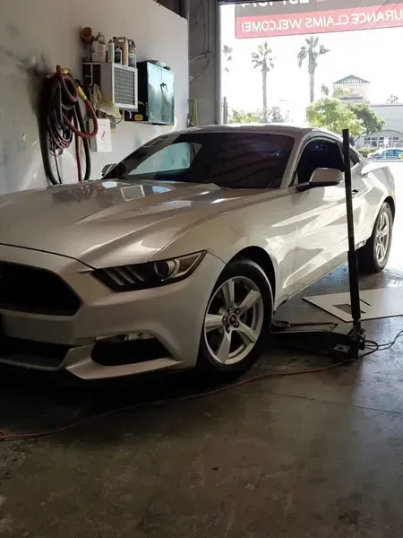 White sports coupe in a garage, connected to a hose or cable, with a wet floor nearby.