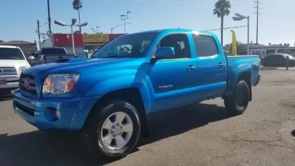 Bright blue pickup truck parked in a sunny lot, side view with palm trees in the background