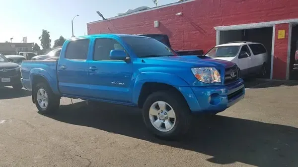 Blue pickup truck parked outside a red building on a sunny day