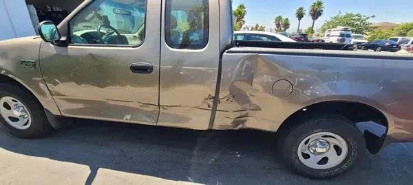 Damaged tan pickup truck with a dented side panel parked on a sunny street