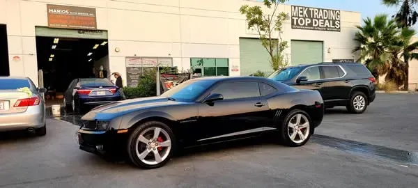 Black sports car parked outside a building with open garage bays and other vehicles nearby