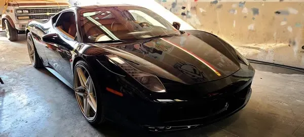 Black sports car parked indoors in a garage, viewed from the front-left side.