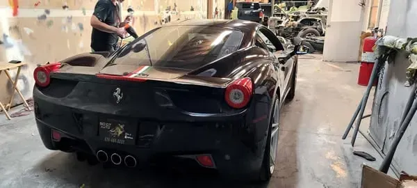 Black Ferrari seen from the rear in a workshop, with a person working on it.