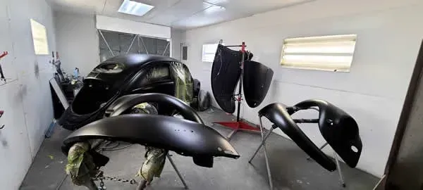 Black car body panels in a white auto body shop with parts hanging to dry