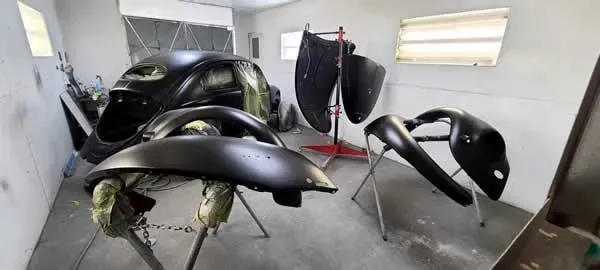 Black car body panels and parts on stands in a white auto workshop.