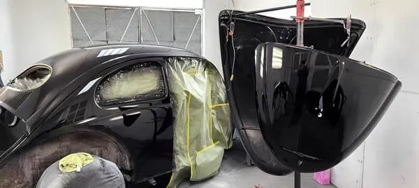 Black car parts and a hood wrapped in plastic inside a workshop booth