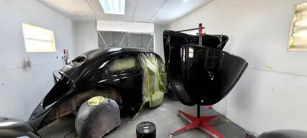 Two black car body panels in a white workshop, one wrapped in green masking film