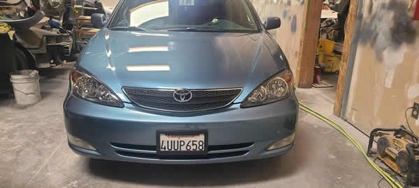 Blue sedan parked inside a garage, front view with headlights and license plate visible