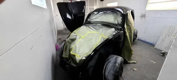 Damaged black car with yellow tape in a narrow indoor garage or workshop