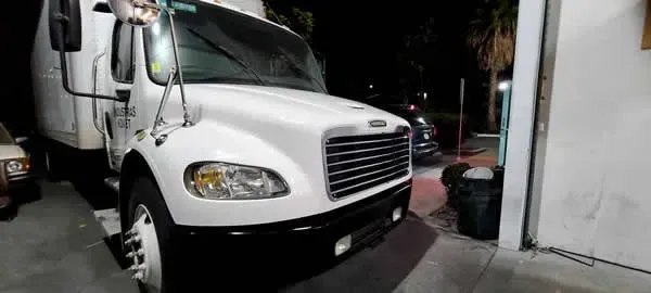 White box truck parked beside a building at night in a dimly lit driveway