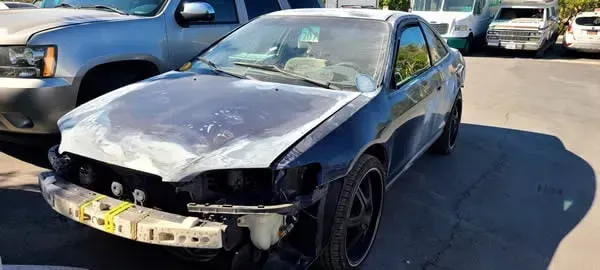 Damaged black sedan with a crumpled hood and missing front bumper in a parking lot