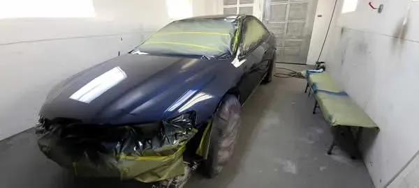 Black sedan parked in a narrow garage, with a bench along the right wall.