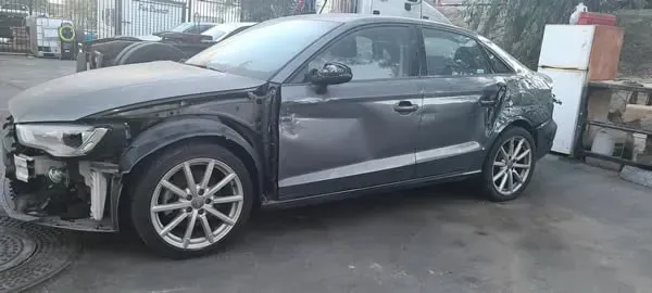 Damaged gray sedan with a smashed front bumper and dented rear quarter panel on a street