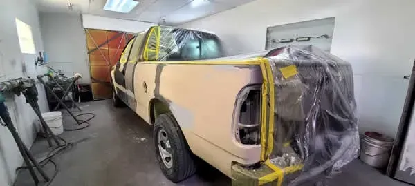 Yellow pickup truck masked with plastic and tape inside a garage, undergoing paint or body repair