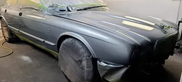 Gray car in a body shop, covered in masking tape and plastic for painting.