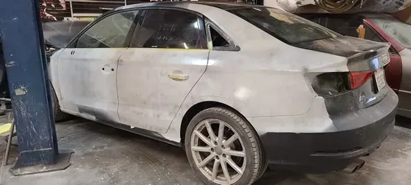 Silver sedan with rear-end damage parked indoors next to a blue car lift