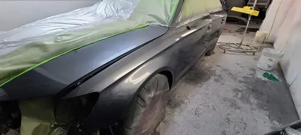 Black car in a garage, partially covered with masking paper and plastic for painting or repair