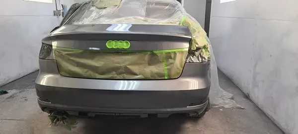 Rear view of a gray car with a greenish-tinted rear window, parked in a concrete bay