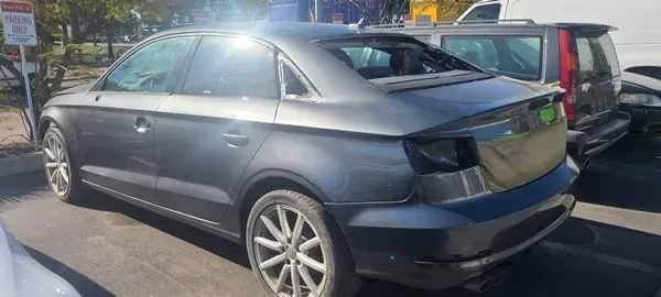 Gray sedan parked in a lot, rear side view, with other cars nearby.