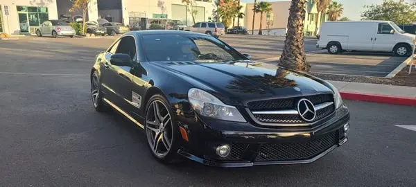 Black Mercedes coupe parked on a street beside palm trees and a white van at dusk