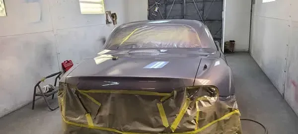 Car primed for painting in a spray booth, front masked with tape and plastic sheeting