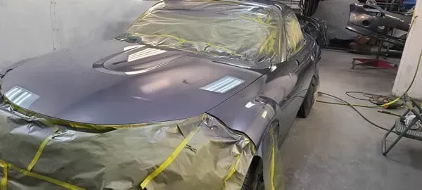 Gray sports car masked with tape and plastic in a body shop during paint preparation