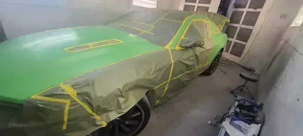 Green car masked with painter’s tape in a garage, being prepped for painting