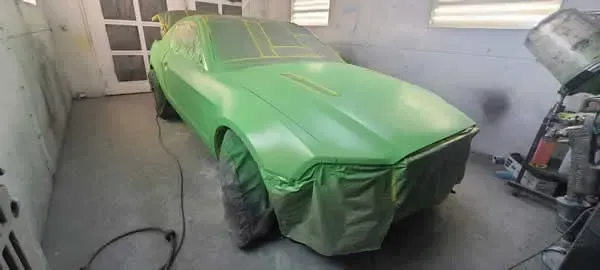Car covered in bright green masking in a garage, ready for paint.