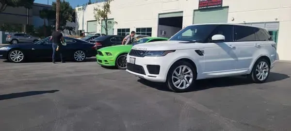 Parking lot with a white SUV in front, a bright green sports car, and a black sedan by a building
