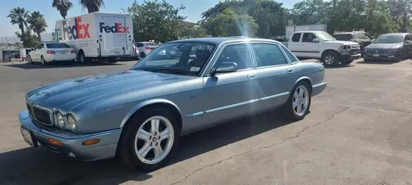 Blue classic luxury sedan parked in a lot with FedEx trucks in the background