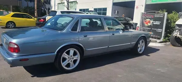Silver classic sedan parked outdoors in a sunny lot, side view