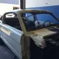 Damaged gray car body with missing hood and front parts in a garage or workshop