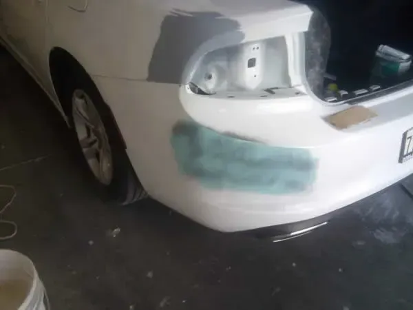 White sedan with rear taillight missing and a green-painted rear bumper in a garage