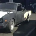 Gray pickup truck parked in a dark garage, with a white rear bed panel missing on one side