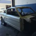Silver classic car body in a garage, front bumper and hood removed, showing unfinished restoration.