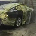 Black car covered in a green tarp inside a garage or workshop