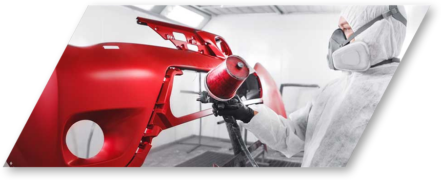 Technician in white protective suit spray-painting a glossy red car body in a paint booth