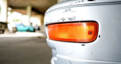 Close-up of a white car’s orange side marker light and rear body panel in a garage