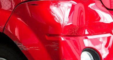 Close-up of a glossy red car hood with a headlight and reflections.