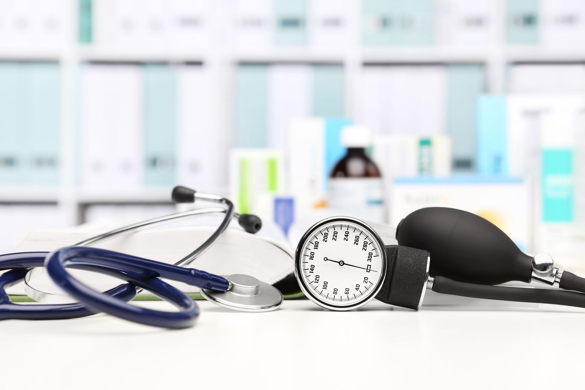 Stetoscopio, bracciale per la misurazione della pressione sanguigna e manometro su una scrivania, con flaconi di medicinali sfocati sullo sfondo.