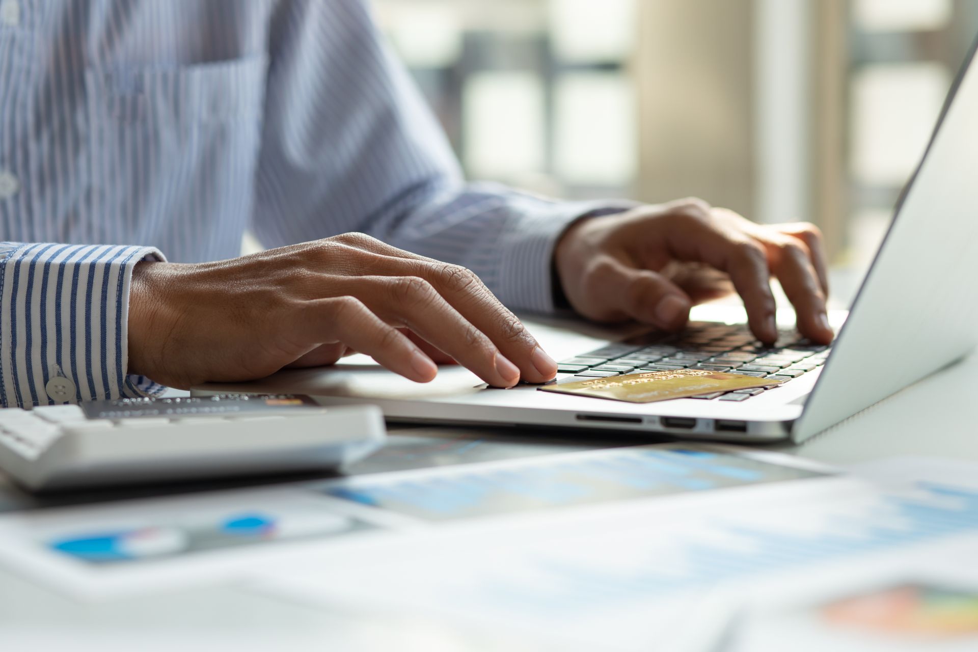 Hands typing on a laptop at a desk with charts and papers nearby