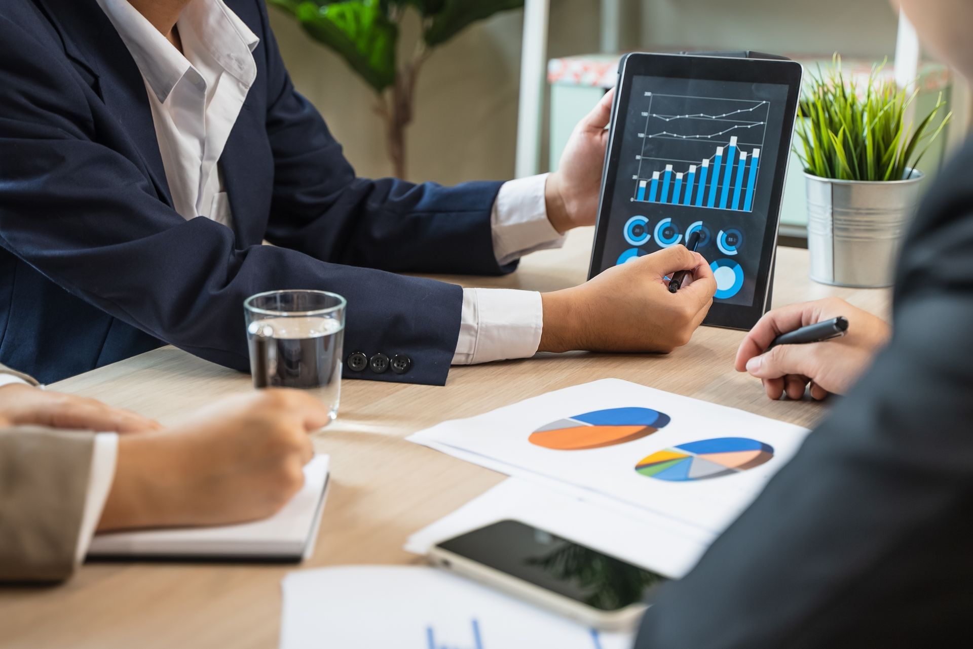 Business meeting with people reviewing charts on a tablet and printed graphs at a conference table
